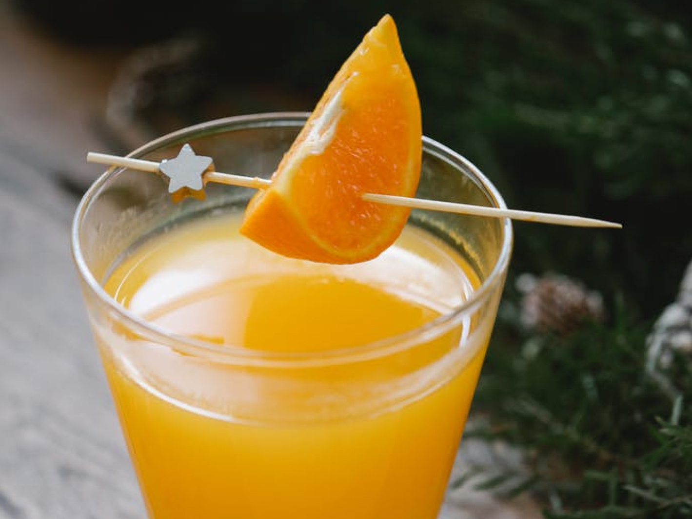 An image of a serving toothpick sticked through a slice of orange on a glass of orange juice